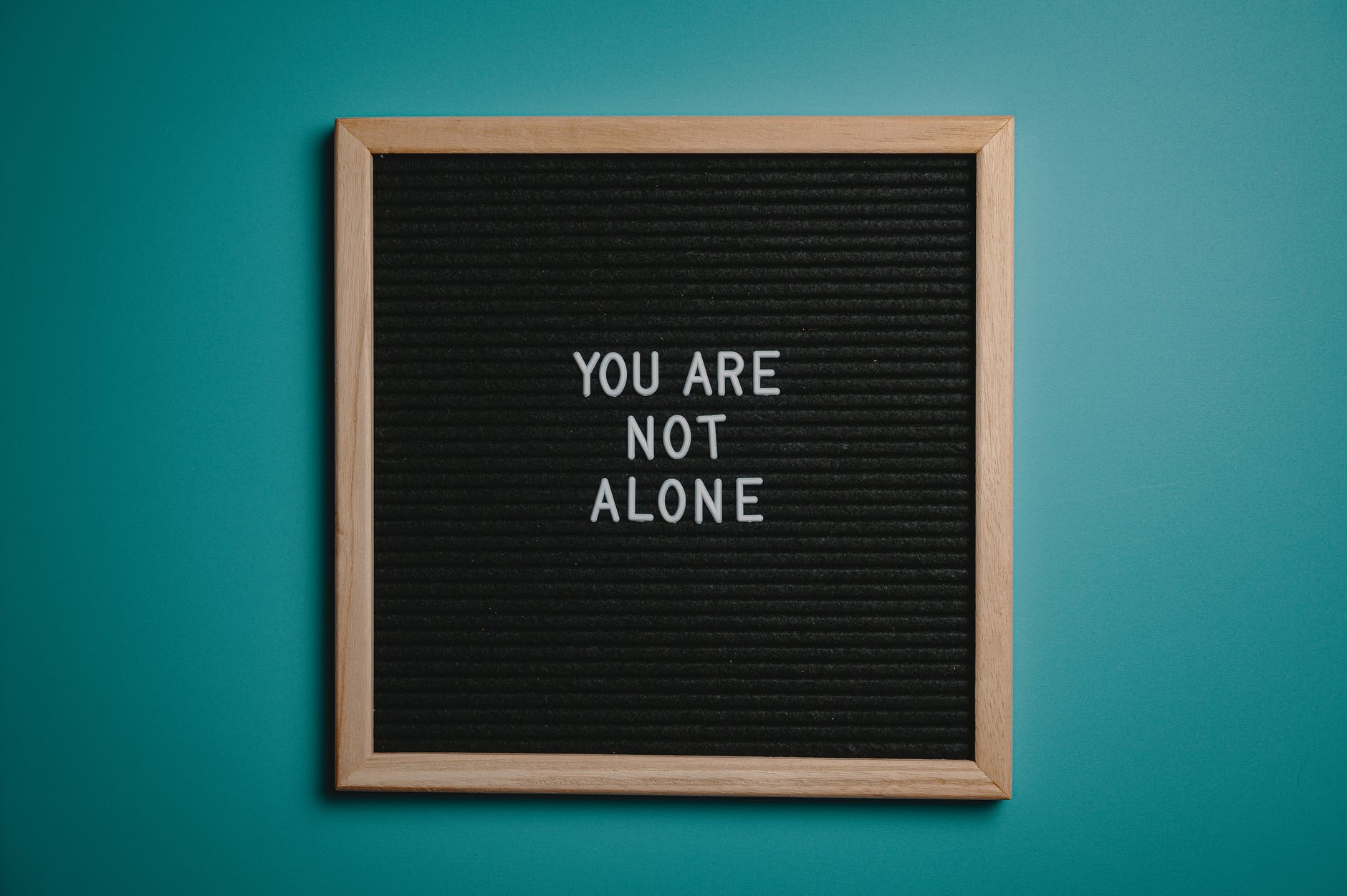 you are not alone quote board on brown wooden frame