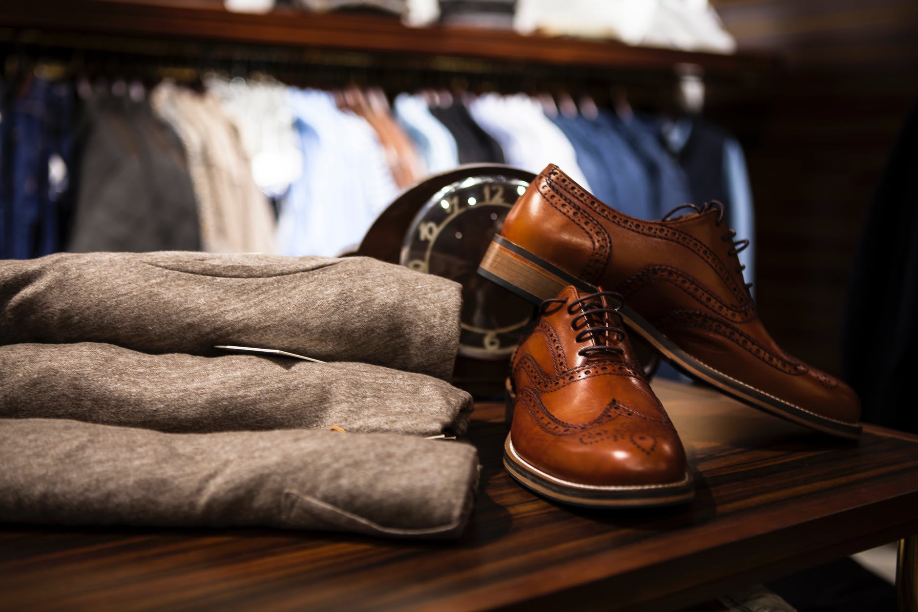 pair of brown leather wingtip shoes beside gray apparel on wooden surface